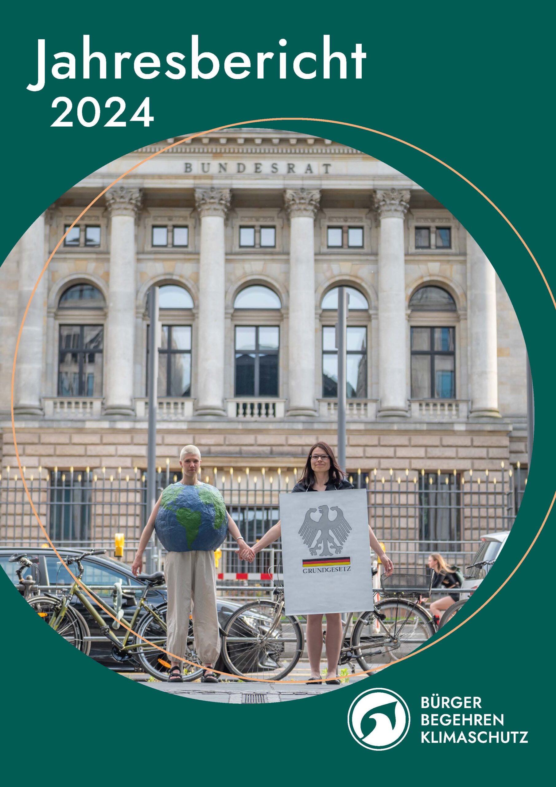 Titelbild des Jahresberichts 2024. Zu sehen ein Bild der Kampagne 'Klimaschutz ins Grundgesetz'. Zwei Menschen als Grundgesetz und Erde verkleidet stehen vor dem Bundesrat und halten sich an der Hand.